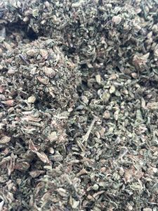 Close-up overhead view of ground green cannabis shake, sugar leaves, and small bud pieces